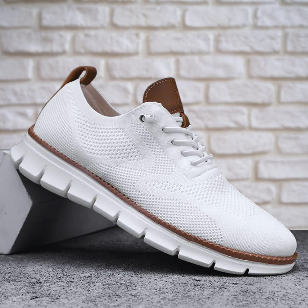 Zapatilla de senderismo blanca con cordones, detalles marrones y suela dentada.