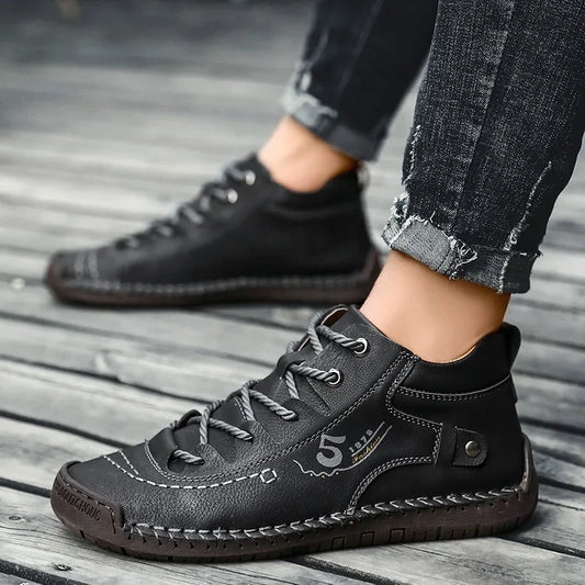 Zapatillas negras con cordones, suela gruesa y costuras decorativas, sobre piso de madera.